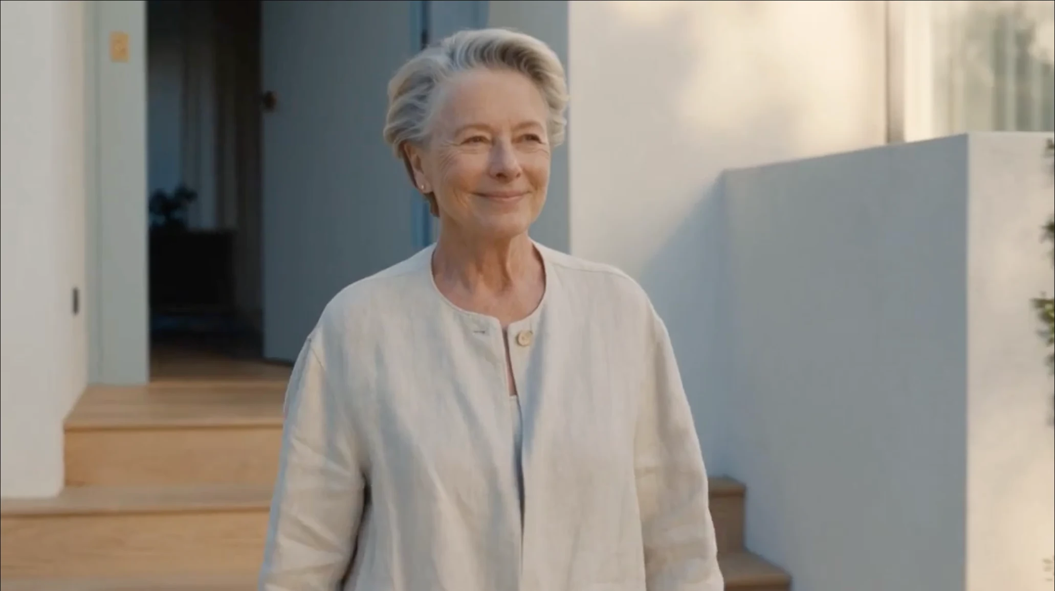 An older woman smiling outside her home in soft evening light