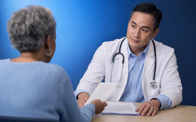 Patient and primary care doctor in conversation at a clinic desk with referral paperwork between them