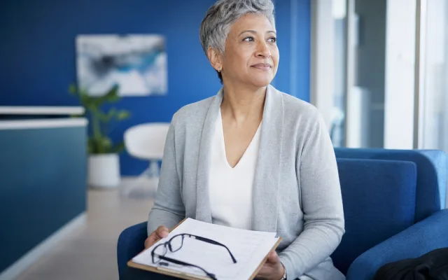 Older adult sitting in a clinic waiting area holding a checklist, calm natural light
