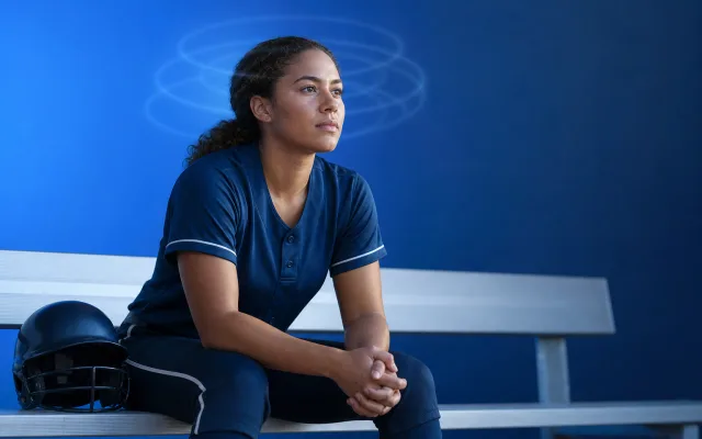 Adult athlete pausing on the sideline with soft overlapping rings of blue light around the head, suggesting cumulative effects of multiple head impacts